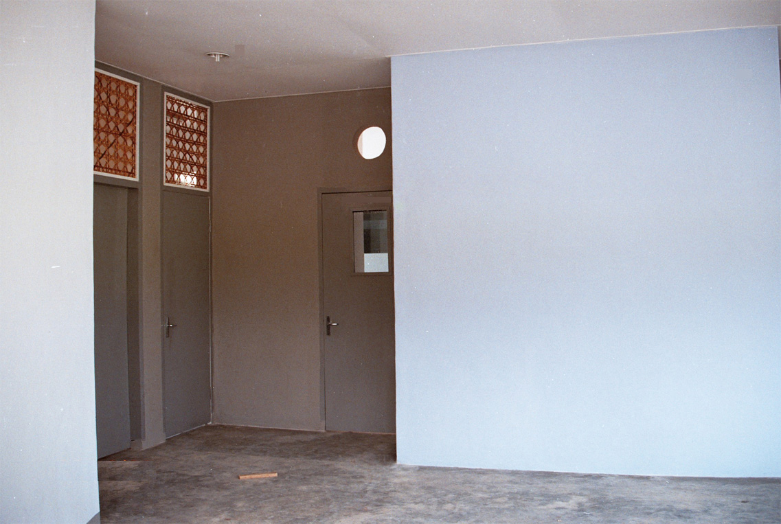 Sol en béton brut, murs bleus et gris, canevas en rotin au dessus des portes pour ventilation naturelle